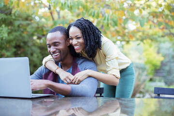Naklejka premium Happy couple using laptop at patio table