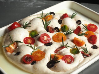 focaccia bread dough with tomato, olive and rosemary in baking tray