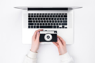 Retro camera in female hands and a laptop on a white background, top view.