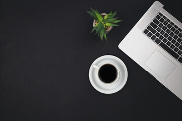 Laptop, coffee cup and office plant on black background, top view.