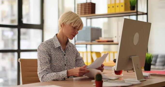 Serious woman sits in office at table and studies documents. Working time and task control in business concept