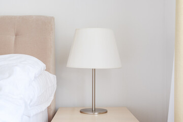 Elegant bedside lamp with white shade on night table in bedroom