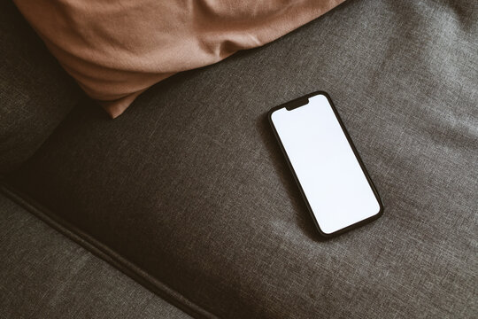 Smart mobile phone device with blank white mockup screen on living room sofa