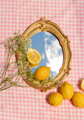 Summer creative layout with vintage mirror with sky reflection and lemons on pink plaid background....