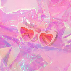 Summer creative background with heart sunglasses on iridescent  pastel colors foil. 80s, 90s retro romantic aesthetic love concept. Minimal fashion cosmetic idea.