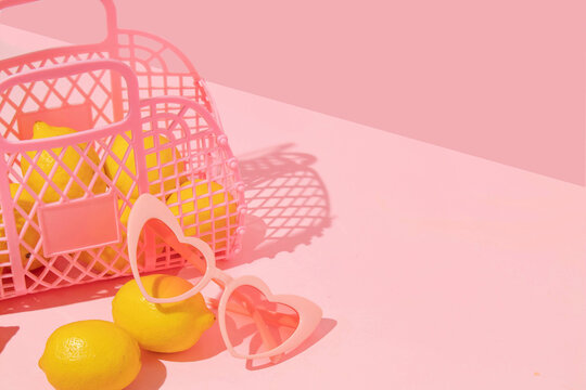 Summer creative layout with pink jelly basket, heart sunglasses with lemons on pink background. 80s or 90s retro aesthetic idea. Minimal summer fruit idea.