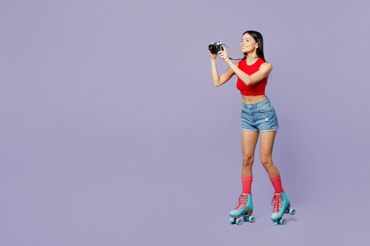 Full body side view young latin woman she wear red casual clothes rollers rollerblading taking photo on photocamera isolated on plain pastel purple background. Summer sport lifestyle leisure concept.
