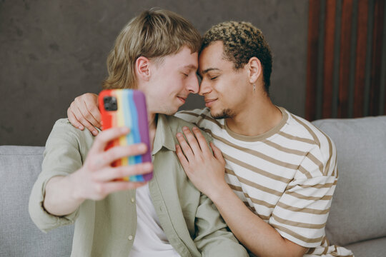 Young couple two gay men wear casual clothes together do selfie shot mobile cell phone hug sit on sofa couch at home flat rest spend free time in living room. Pride day june month love lgbtq concept.