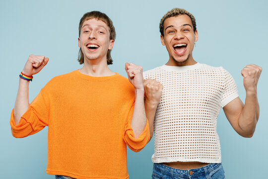 Young happy couple two gay men wear casual clothes together do winner gesture celebrate clench fist isolated on pastel plain light blue color background studio Pride day june month love LGBTQ concept