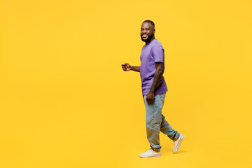 Fototapeta na wymiar Full body side view young man of African American ethnicity he wear casual clothes purple t-shirt looking camera walk go stroll isolated on plain yellow background studio portrait. Lifestyle concept.