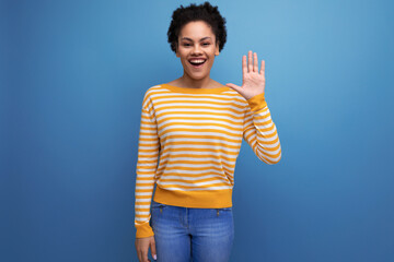 positive brunette latin young woman with ponytail in yellow sweater on studio background