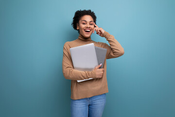 young beautiful hispanic student lady with afro curly hair in casual clothes holding laptop on background with copy space