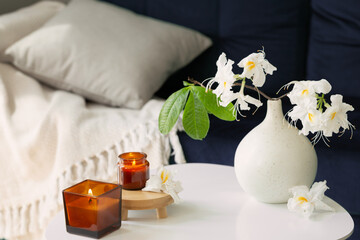 branch of white rhododendron in vase and burning candles  in modern cozy interior