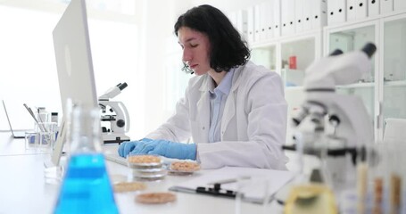 Handsome young laboratory assistant using computer working in laboratory and analyzer of cereals and grains. Research chemistry and eco products check for toxins