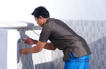 An Asian Muslim man is wudhu in the washroom.