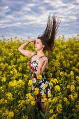 Naklejka na ściany i meble Beautiful latino woman in floral dress in a canola field