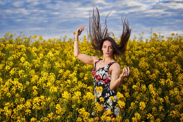 Naklejka na ściany i meble Beautiful latino woman in floral dress in a canola field