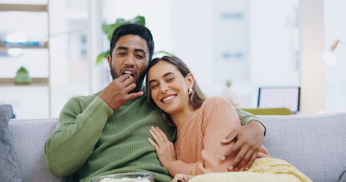 Happy couple, hug and relax watching tv with popcorn for entertainment or streaming on living room sofa at home. Portrait of man and woman relaxing, hugging or eating with remote for movie on couch