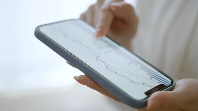 スマートフォンで為替チャートを確認する女性の手元
