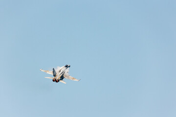 Top rear view of an F-18 jet fighter in Gijon Air show festival ascending at sonic speed in a clear...