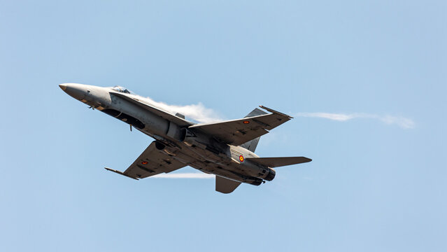 Front bottom view of an F-16 jet fighter in an Air show festival ascending at sonic speed in a clear blue sky with condensation big wakes in its wings - Powered by Adobe
