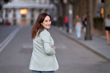 Woman looking back to camera and smiling while walking outdoors on the street.