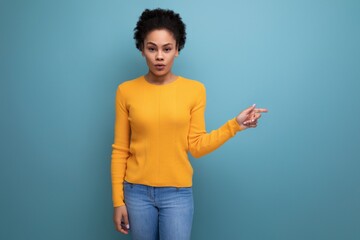 pretty surprised young latin woman with afro hair showing hand to side on studio background