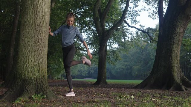 Young Caucasian woman runner stretching in a forest during a crisp morning workout. Tracking shot capturing her dynamic energy