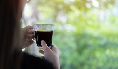 Asian woman hand holding the glass of coffee in the morning at home on green nature background.