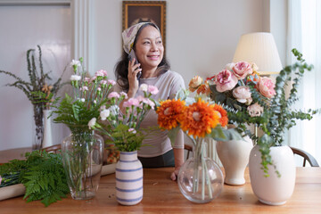Startup, small business, flower shop. Older florist putting a flower on a vase and talking with customer by phone