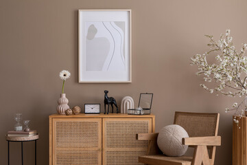 Spring composition of cozy living room interior with mock up poster frame, rattan sideboard, wooden armchair, round pillow, sculpture, cherry blossoms and personal accessories. Home decor. Template.