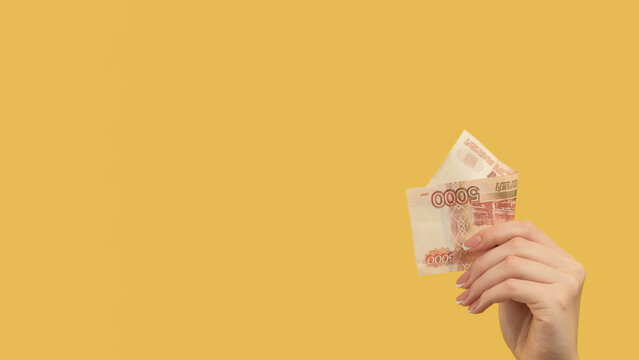 Passive income. Money gesture. Female hand holding russian rubles 500 on yellow background copy space.