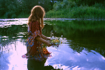girl near river and holding flower wreath, abstract natural background. esoteric ritual for summer...