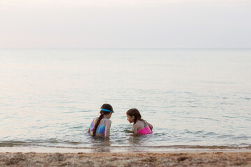children girls swim in sea in evening at sunset