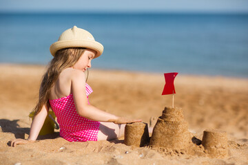 baby child in hat sits on beach against background of sea and plays sand, builds castle. vacation...