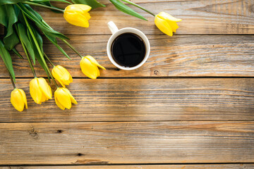 Bouquet of yellow tulips and cup of coffee on a wooden background, top view.