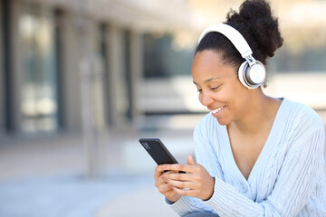Happy black woman listening to music in the street with phone