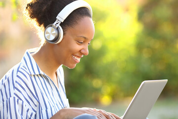 Happy black woman watching media on laptop with headphone