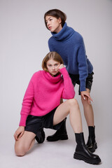 Two fashion models in pink fuchsia and blue sweater, blouse, black leather shorts. Beautiful young woman. Studio shot, portrait. White background. Asian and  blonde. 
