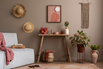 Living room interior with mock up poster frame, wooden consola, gray sofa, plants in flowerpots, basket with pink plaid, macrame, beige wall and personal accessories. Home decor. Template.