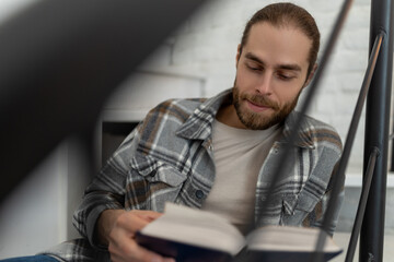 Man reading book while sitting on stairs in his apartment.