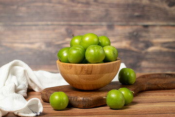 Green plum in bowl. Organic farm products. Fresh plum on wooden background