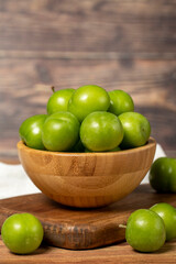 Green plum in bowl. Organic farm products. Fresh plum on wooden background. Close up