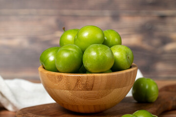 Green plum in bowl. Organic farm products. Fresh plum on wooden background. Close up