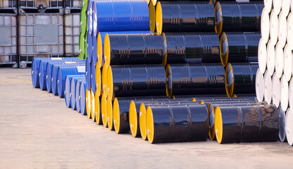 Pile of many various oil drums stacked on industrial yard area in perspective side view
