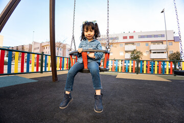 A cute little girl between 3 and 4 years old is sitting on a children's seesaw in an outdoor park. Concept of fun in African girls. Have fun on playgrounds, swings on playgrounds.
