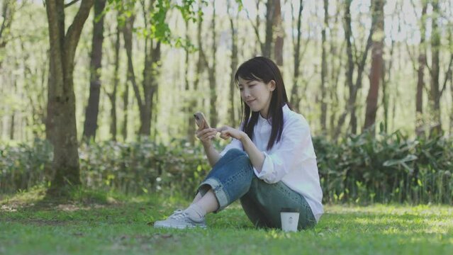森の中でリラックスしながらスマートフォンを操作する30代日本人女性の初夏のイメージ