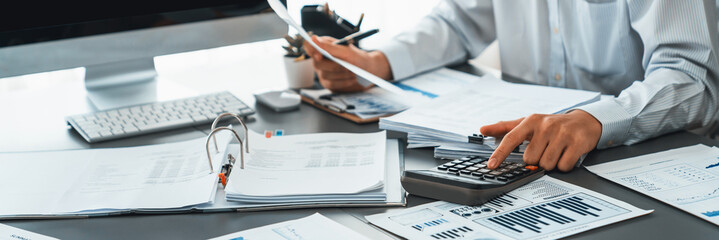 Corporate auditor calculating budget with calculator on his office desk. Dedicated accountant professional of accounting business company analyzing financial document to forecast income. Insight