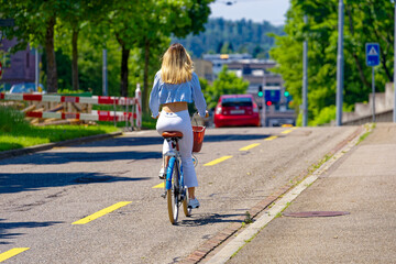 Urban road with bicycle lane and young stylish woman riding old fashioned bicycle with basket at...