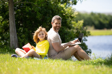 Father and son reading book in park, man encourages boy to knowledge, family education. Father and child read book together outdoor. Happy parent reading with child book on summer nature in park.